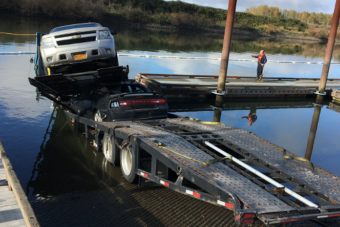 Car hauler gets pummeled by a train, then crashes down a boat ramp into a lake
