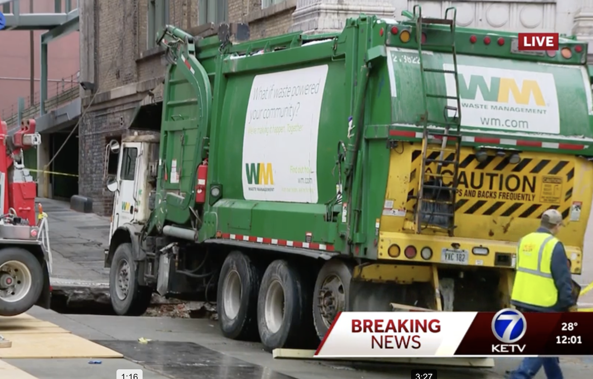 Garbage truck partially swallowed by alleyway sink hole after driver drags away barricade