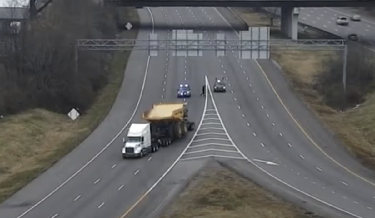 Trucker with oversize load avoids striking railroad bridge by reversing onto on-ramp