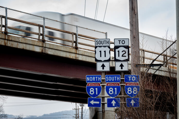Tractor Trailer rushes by on overhead on Rt 81 in Binghamton in Broome County in Upstate NY. Road signs show the way to major Routes. Major highways cross at this part of Castle Creek Rd.