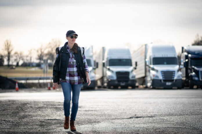 Woman commercial truck driver walking in trucking yard Female truck driver