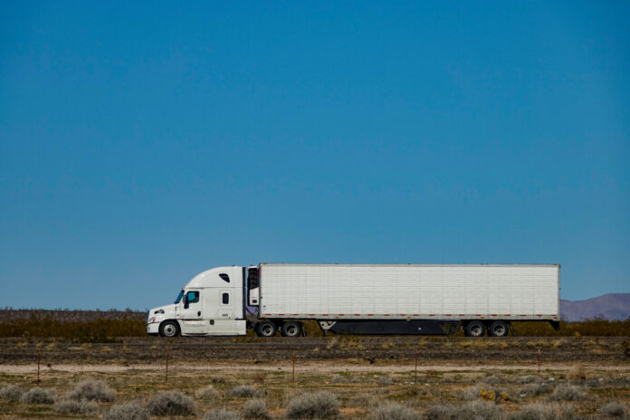 CLOSE UP: White semi-trailer truck hauls a container across a desert in the USA.