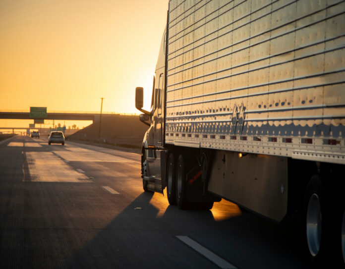 Long Haul 18 Wheel Truck driving on a highway at sunrise or sunset